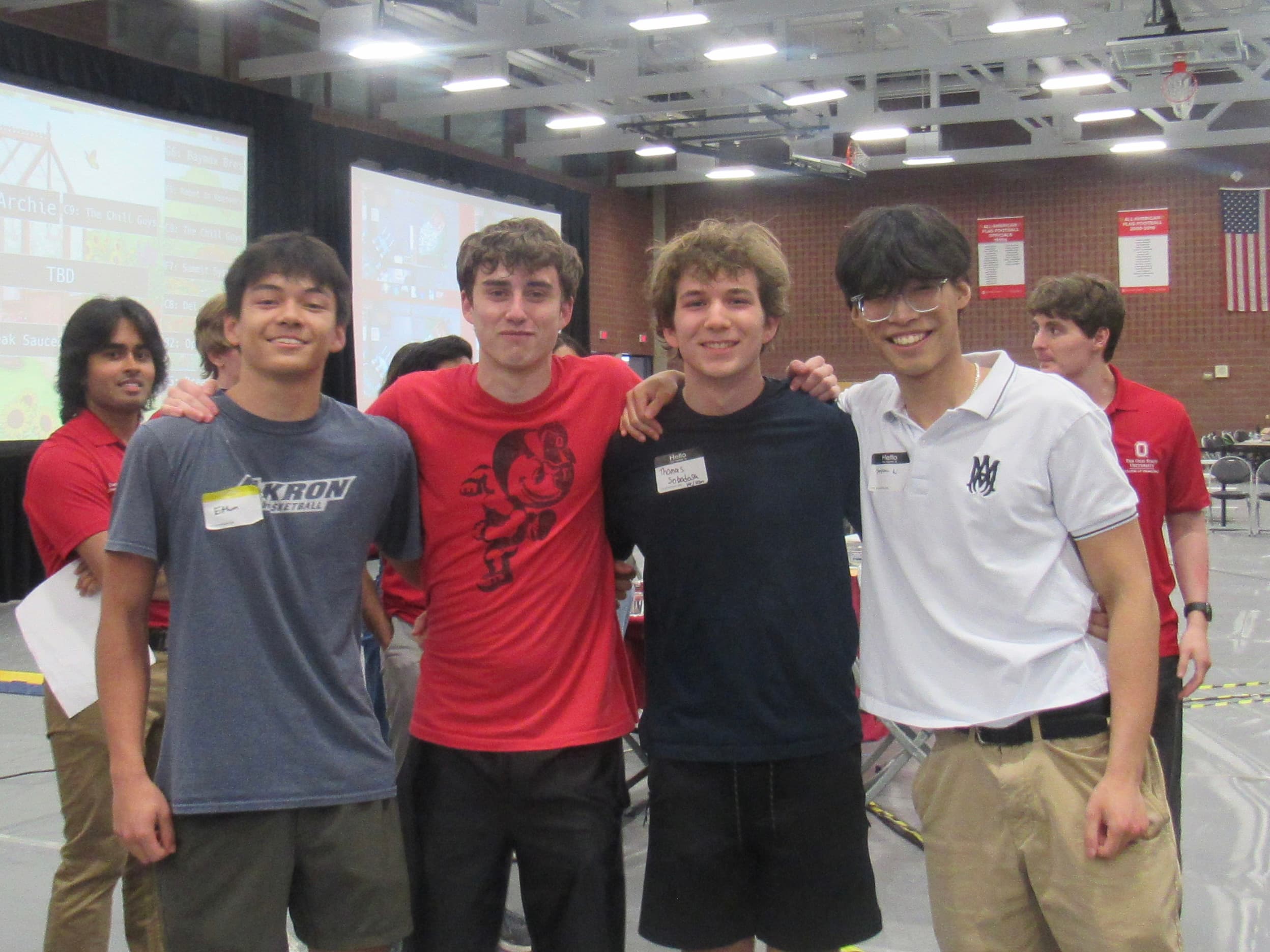 The four members of Group C9 standing together at the showcase, arms around each other's shoulders, wearing name tags.